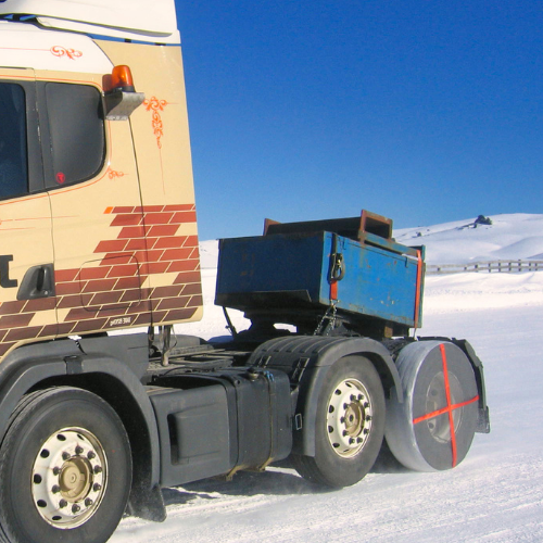 AutoSock für LKW beim Fahren, montiert auf Hinterrad eines LKW auf schneebedeckter Fahrbahn in Winterlandschaft